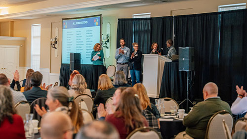 Employees sit at tables during an award presentation on stage