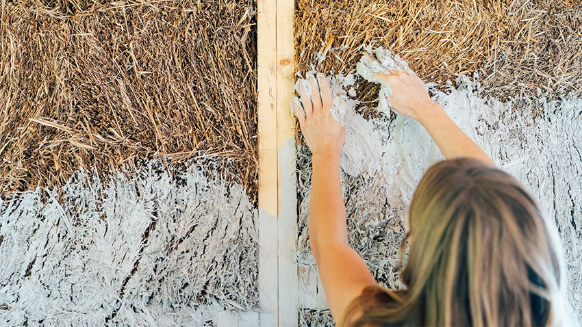 woman applies paste to straw walls