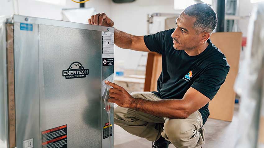 Shaker Manns kneels down to inspect an electrical box inside a newly redeveloped apartment