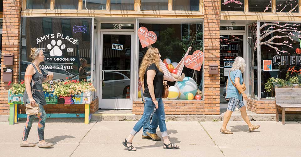 A group of women walk the sidewalk in front of several small business in Lapeer, MI